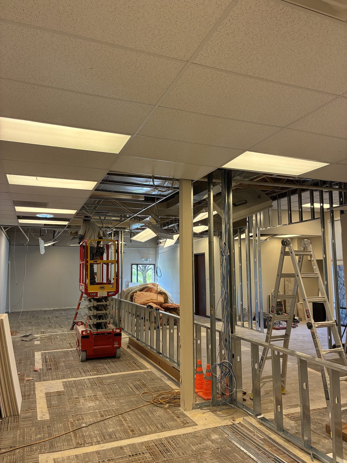 Scissor lift and steel stud wall framing beneath an open suspended ceiling grid during a commercial office build-out in Boise
