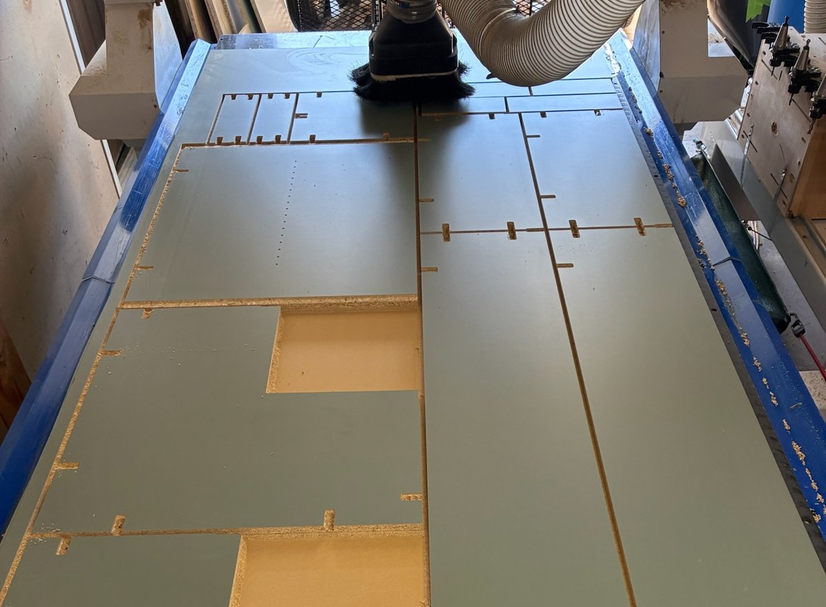 Nested cabinet parts mid-cut on a 4x8 CNC, tabs still holding every part to the melamine sheet