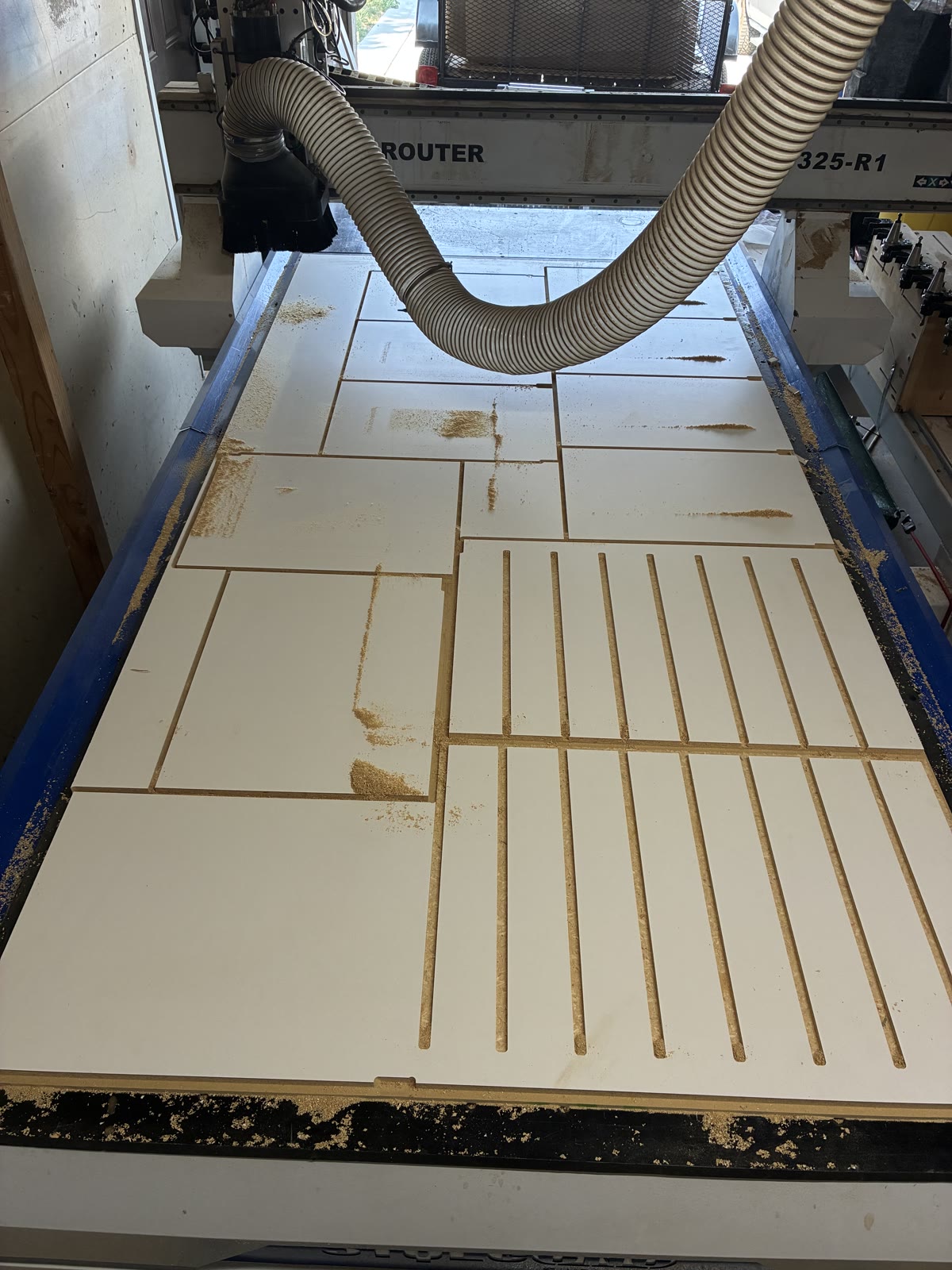 White-faced sheet material on a CNC router bed with parallel slots cut into two rectangular panels