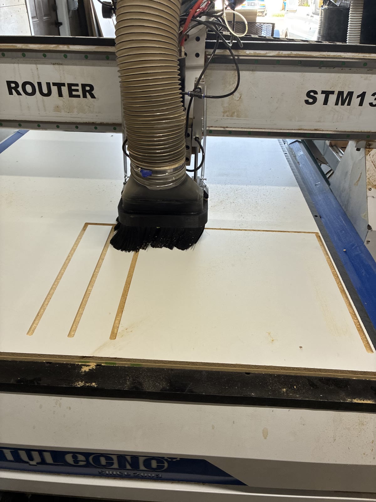 CNC router dust hood over a white-faced panel with parallel slots